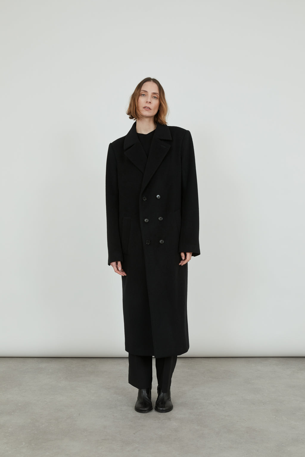 A person wearing a double-breasted, double-face black cashmere Achilles coat.