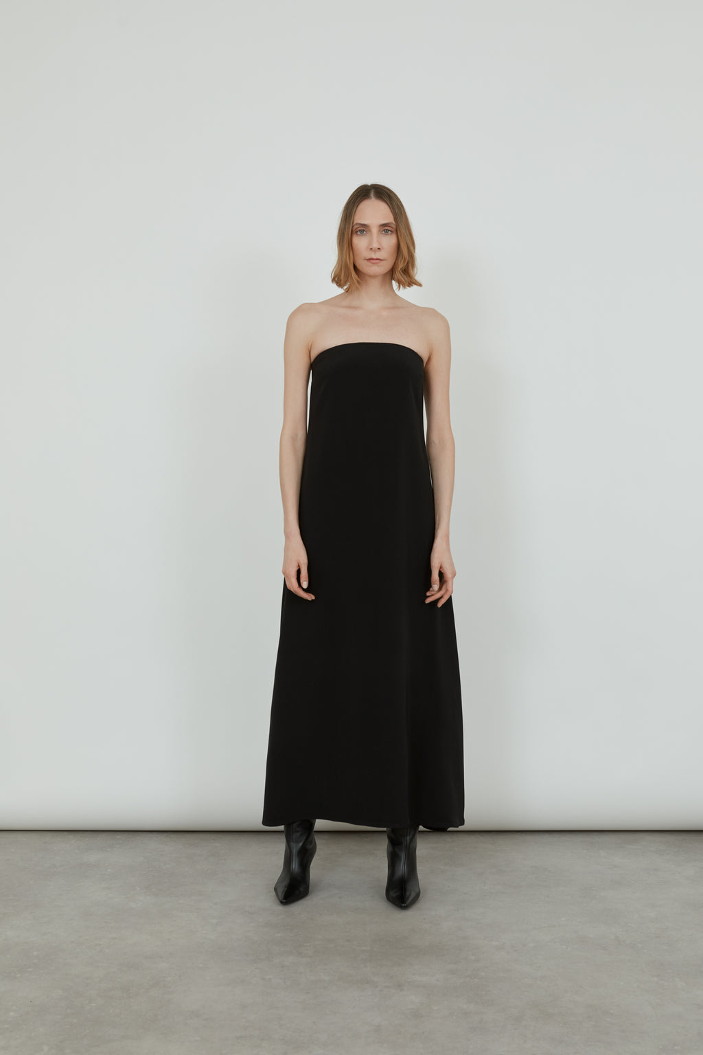 Woman wearing a black bandeau dress with black pointy boots.