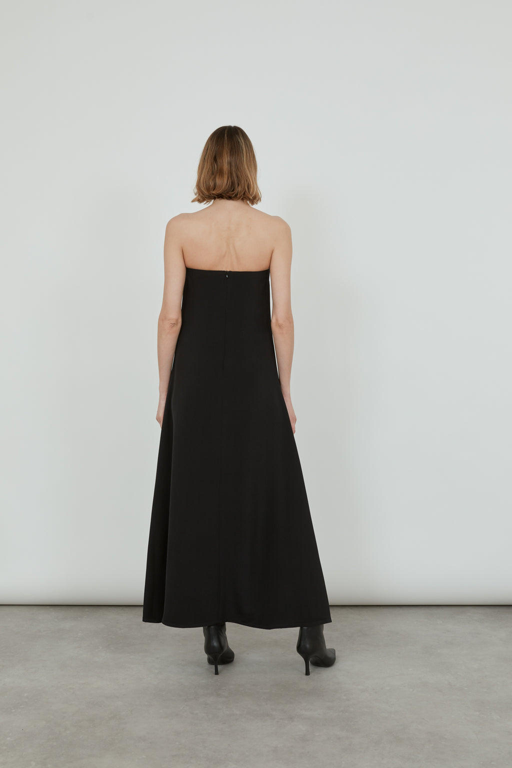Woman wearing a black strapless dress with black pointy heeled boots showing her back.