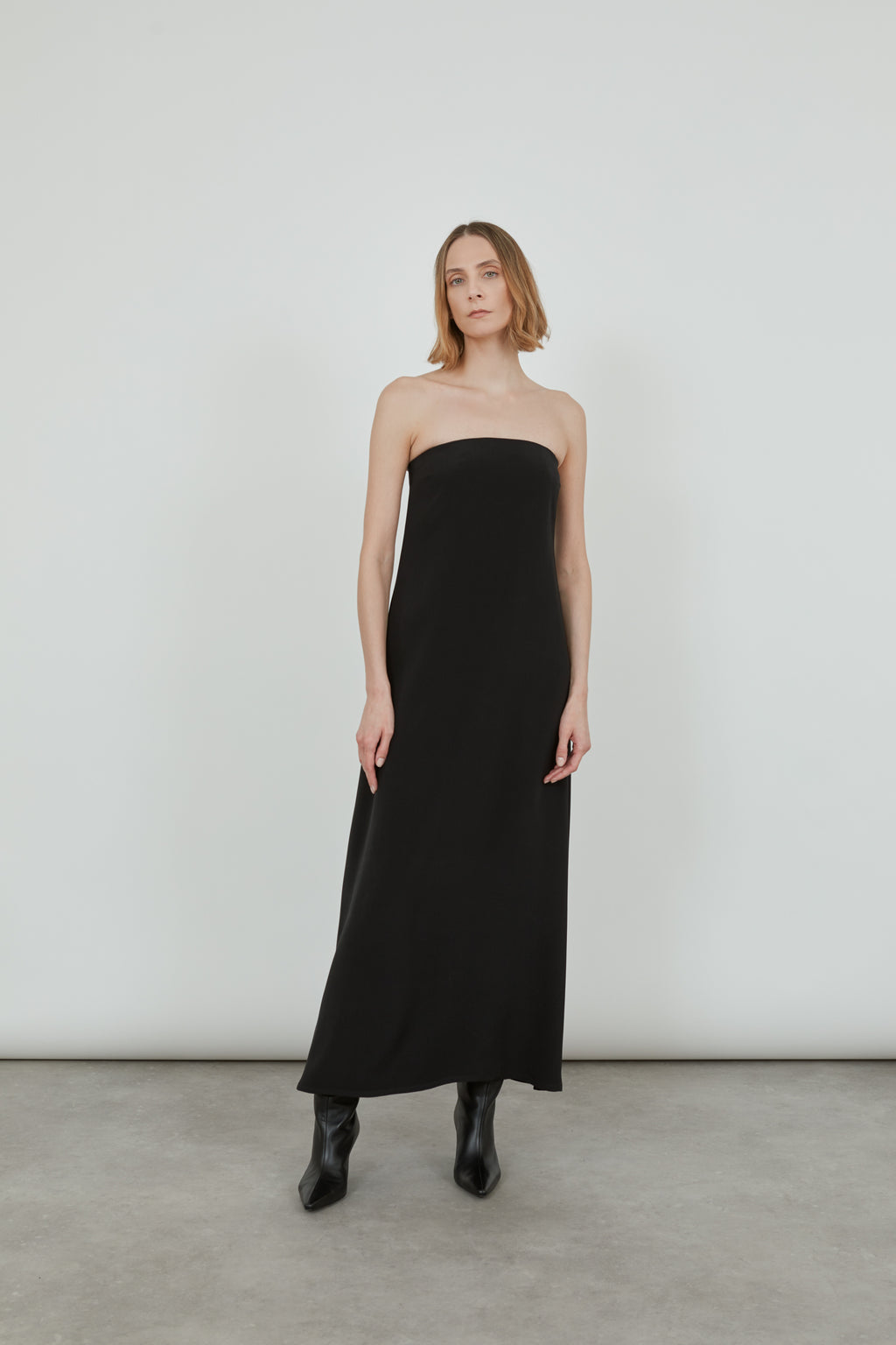 Woman wearing a black strapless dress with black pointy boots..