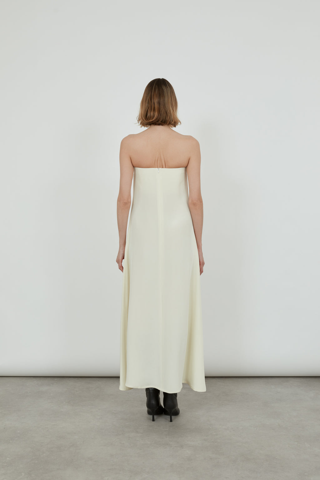 Woman standing with her back to the lens, wearing an off white strapless dress. 