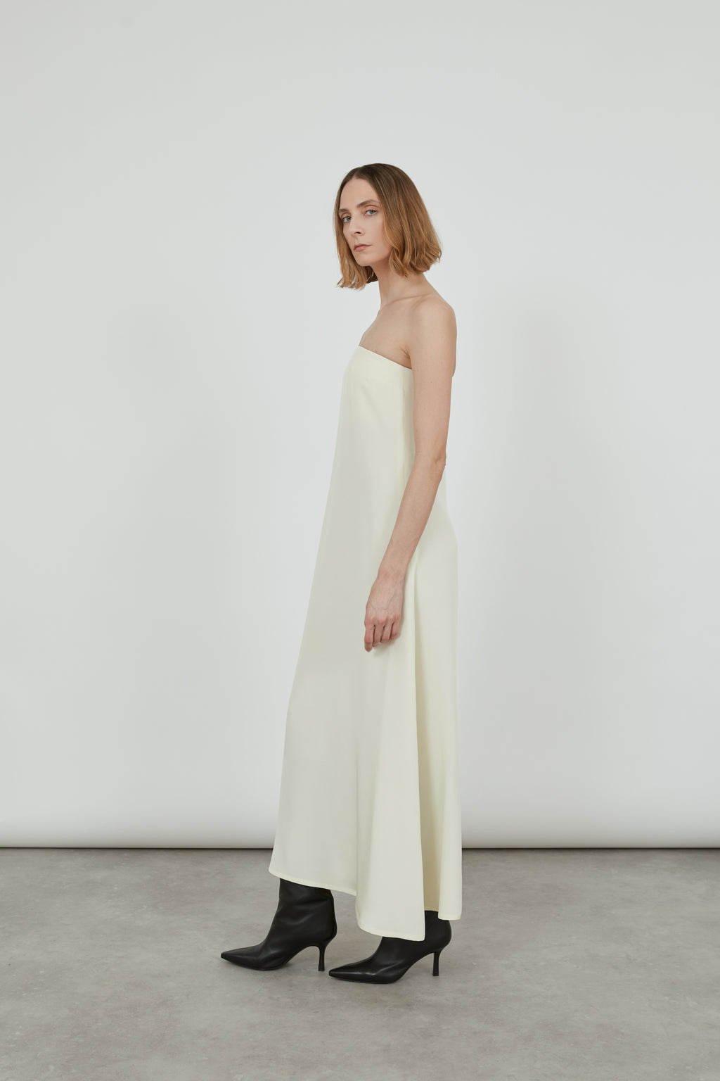 Woman wearing a cream bandeau dress standing with her side to the camera.