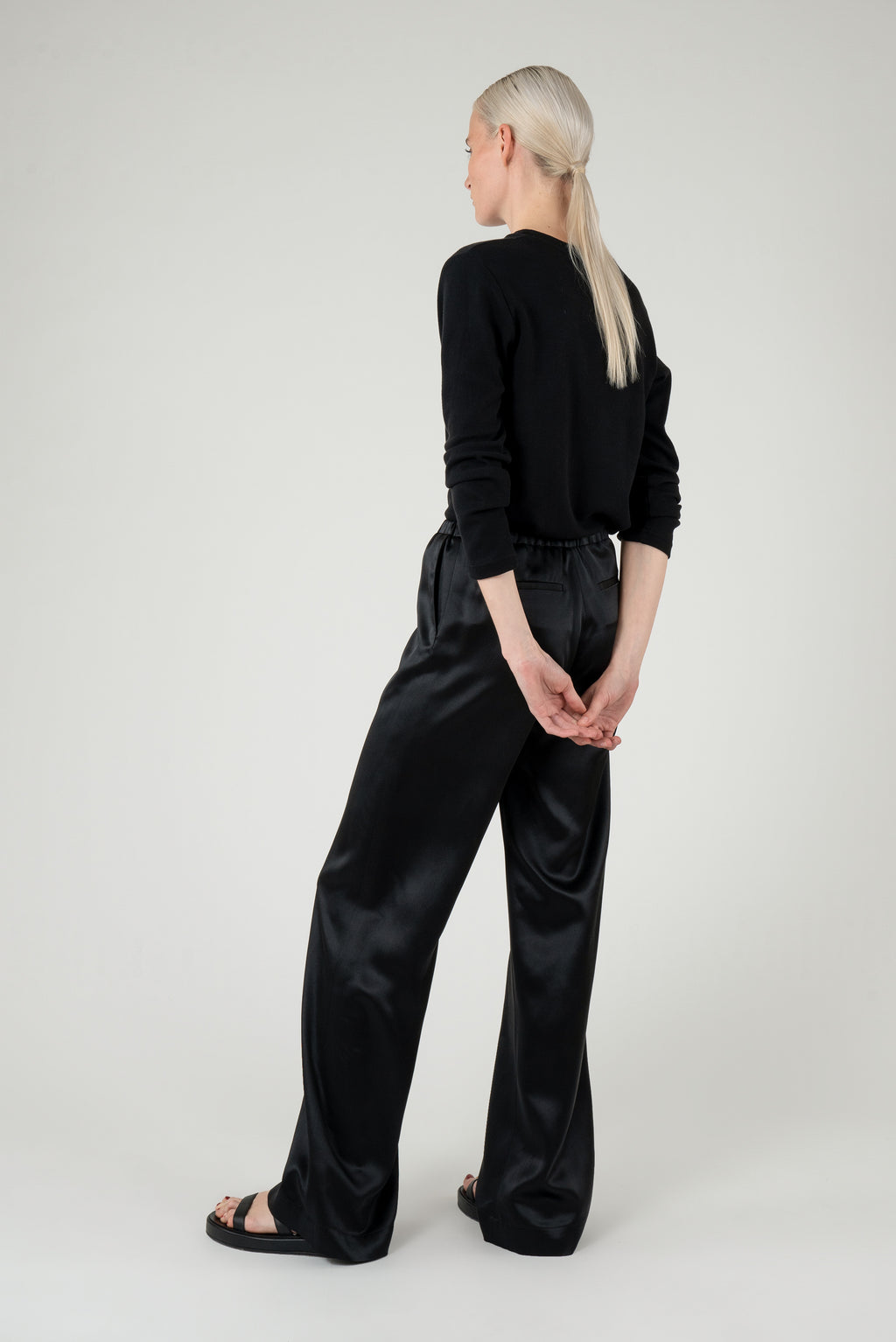 Woman wearing a black longsleeve top and a black satin pants showing her back.