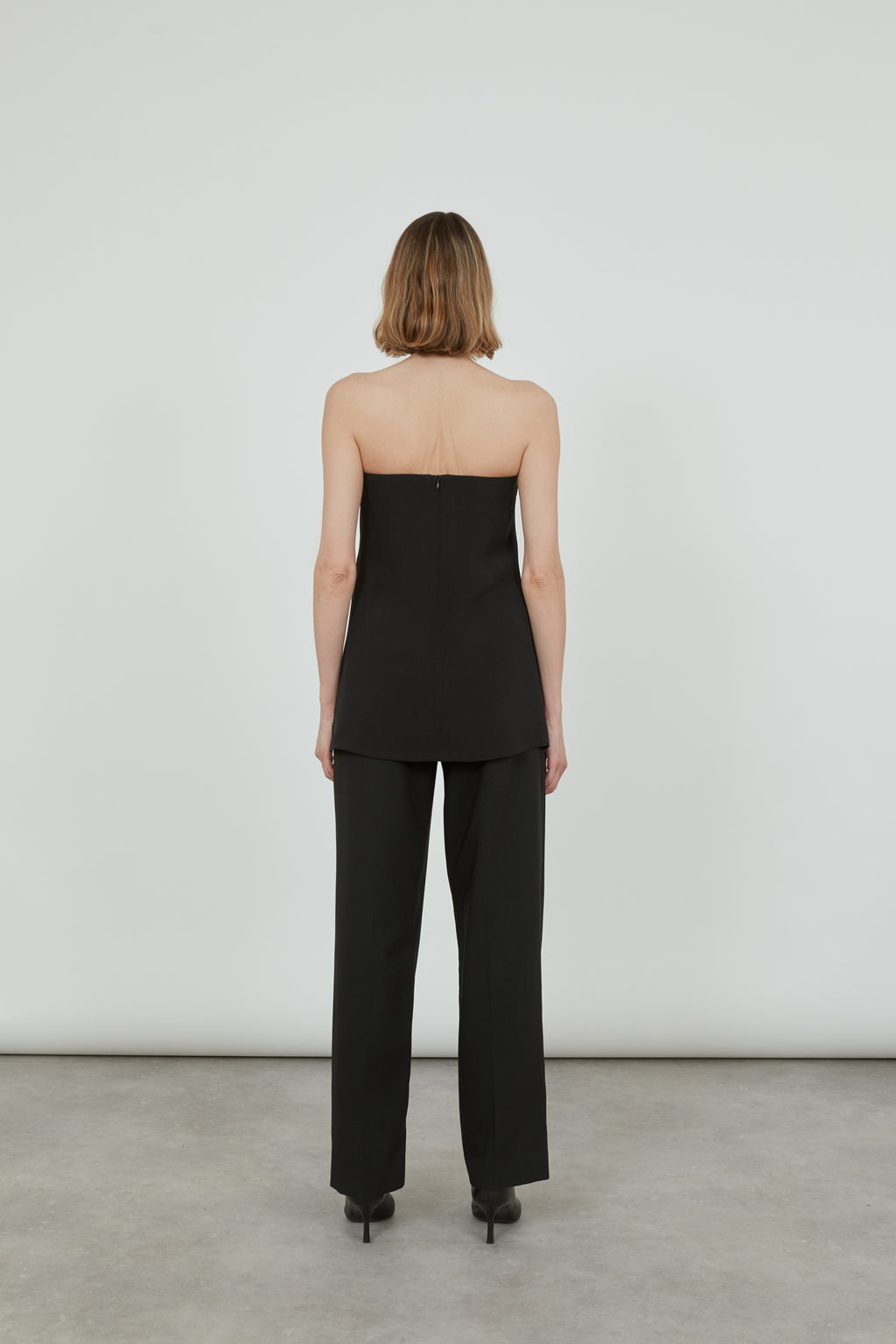Woman wearing a black strapless top, showing the back of the top.