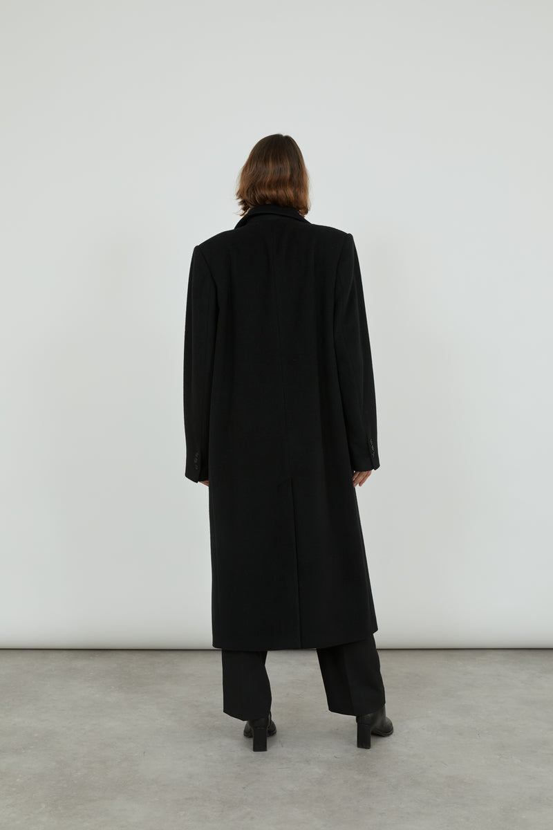 A person wearing a black cashmere Achilles coat standing with her back to the camera.