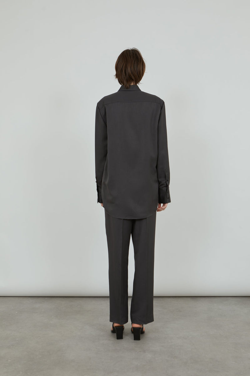 woman wearing grey viscose shirt and trousers standing with her back to the camera.