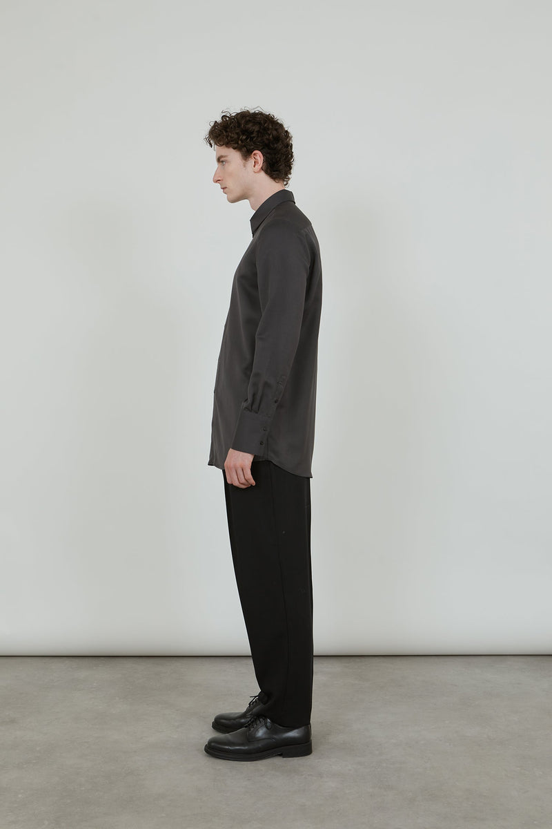 Man standing sideways wearing an aubergine grey shirt and a black wool trousers.