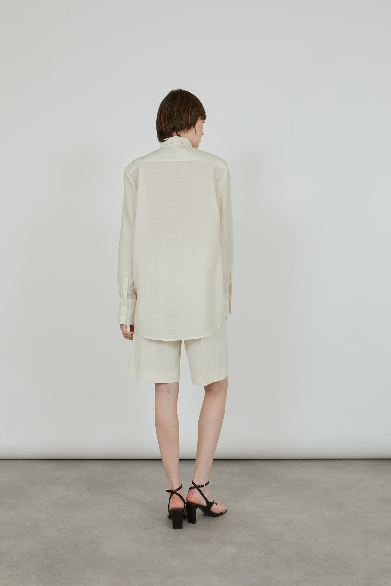 Woman wearing an all off white look, wool wilk blend shirt and cool wool shorts with heeled sandals. 