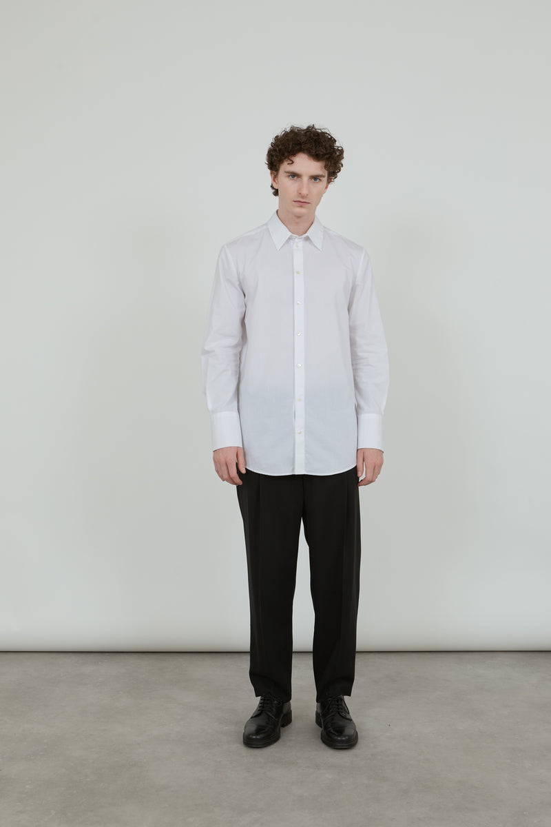 Person wearing a classic white Adam shirt in cotton poplin, with classic black pants and black leather shoes.