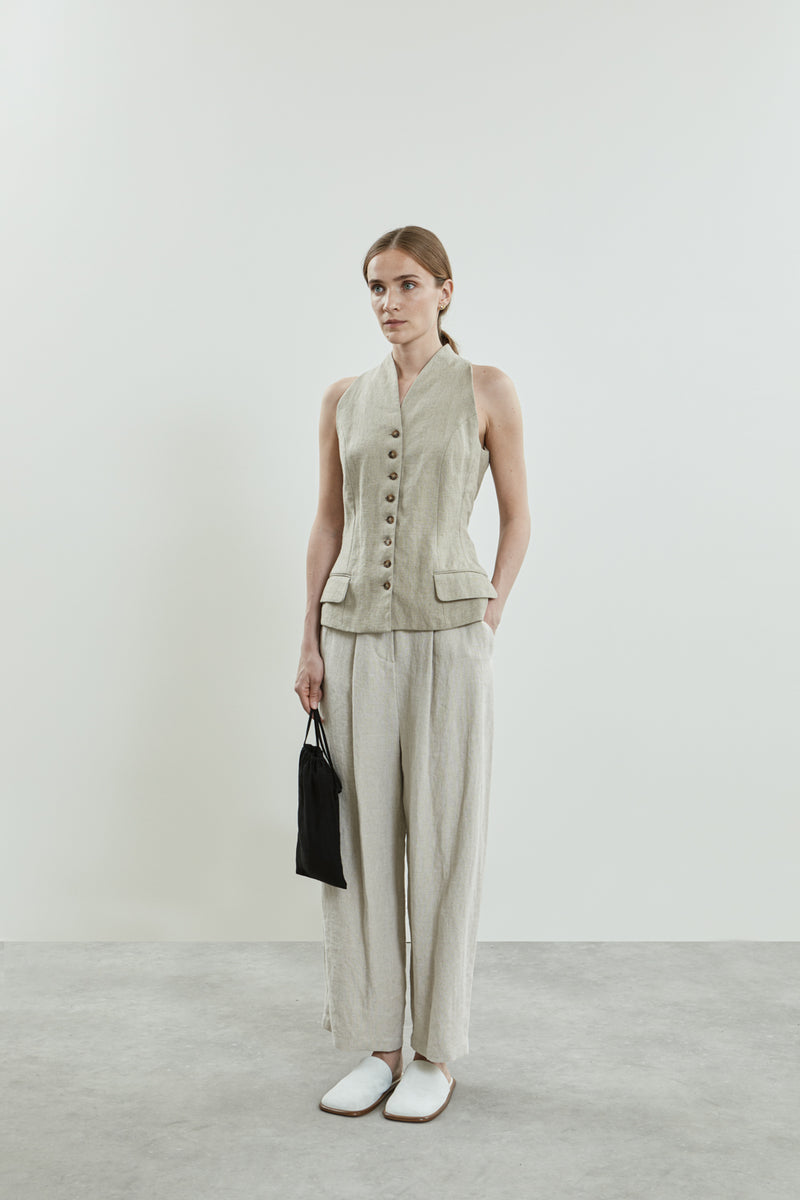 Full-length view of the beige Akari gilet, featuring a structured neckline, sharp button fastening, and flap pocket.