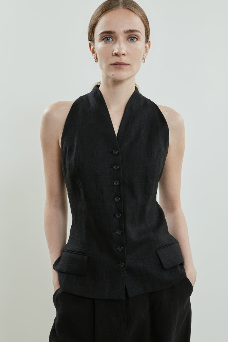 Close-up of the detailed button fastening and flap pockets on the black Akari gilet, made from lightweight linen.