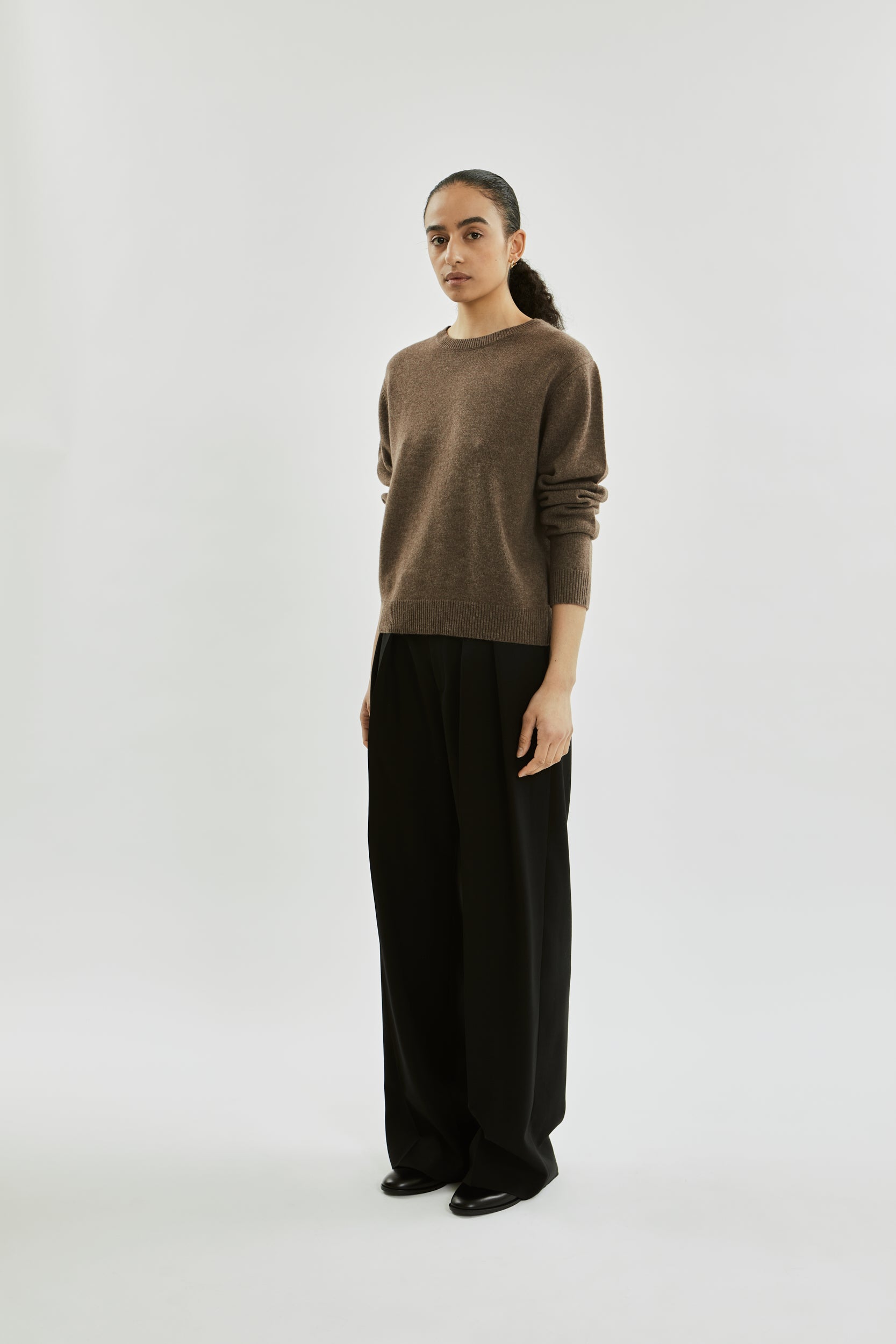 Person wearing a brown sweater and black pants on a white background