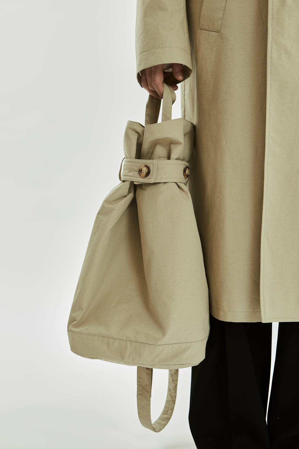 Person holding a beige drawstring bag with a matching trench coat on a white background