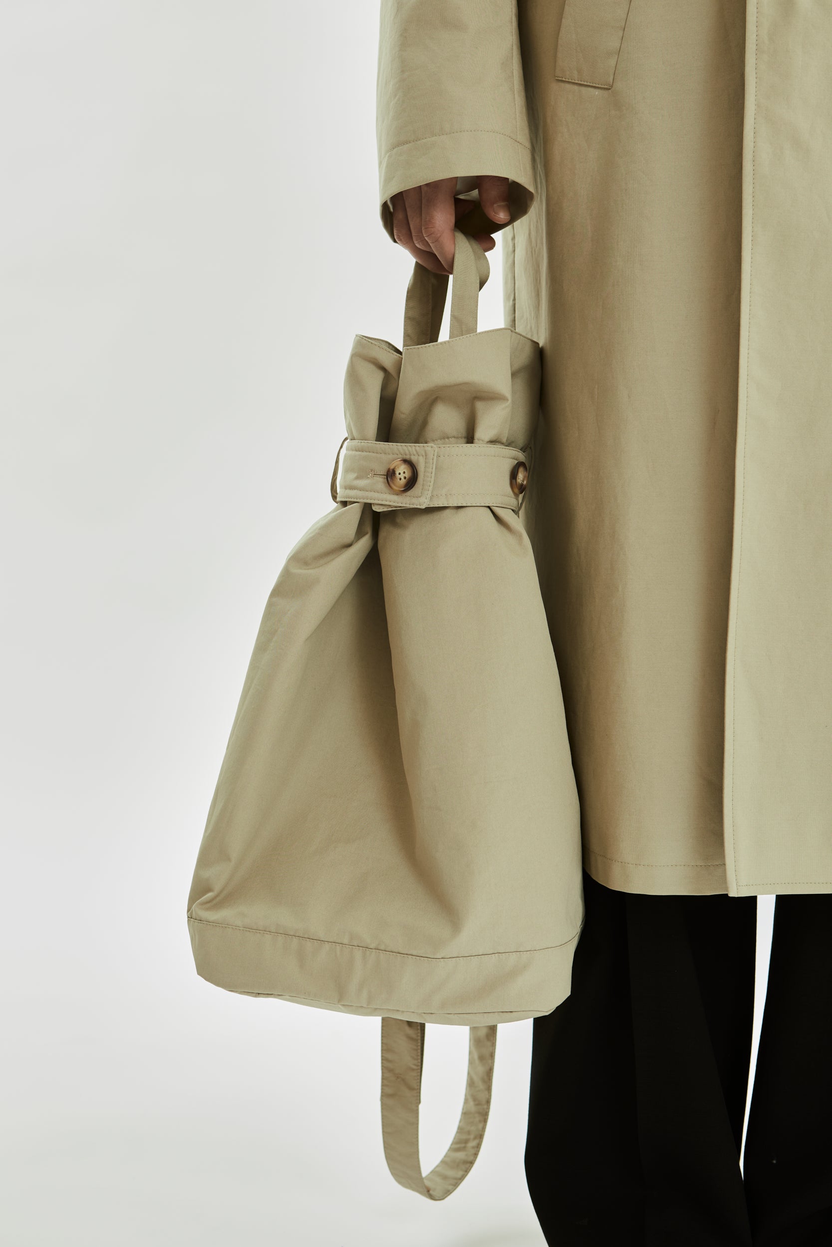 Person holding a beige drawstring bag with a matching trench coat on a white background