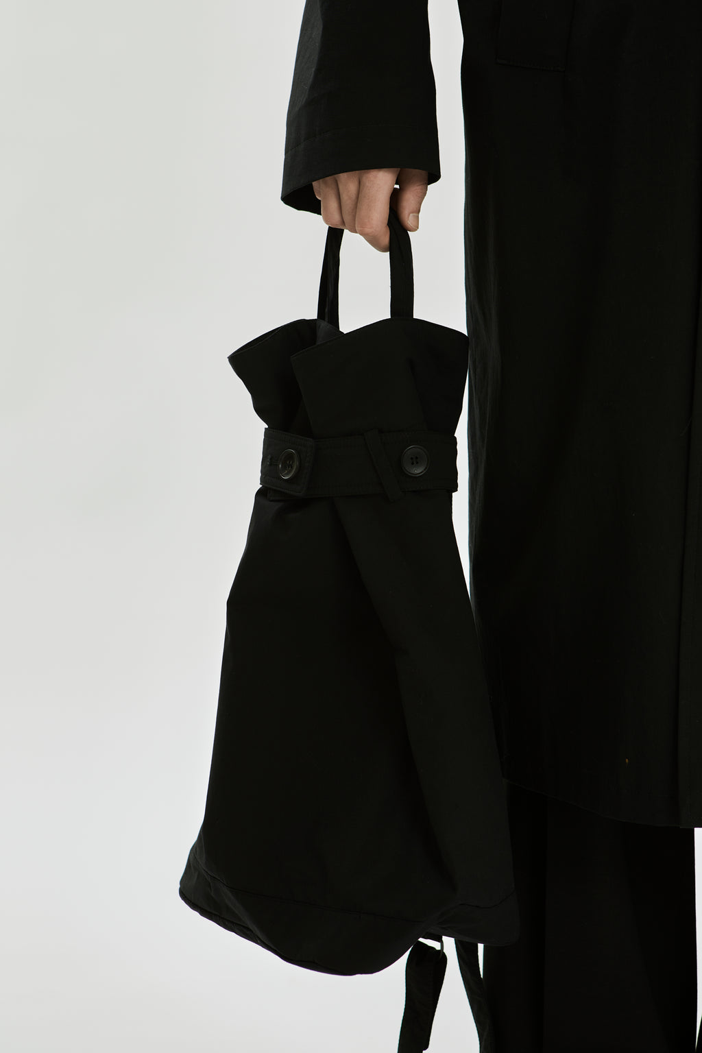 Person holding a black tote bag against a plain background