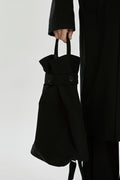 Person holding a black tote bag against a plain background