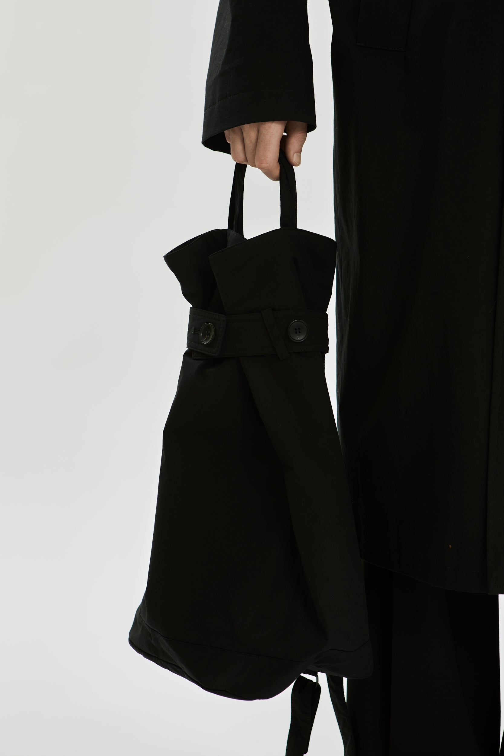 Person holding a black tote bag against a plain background