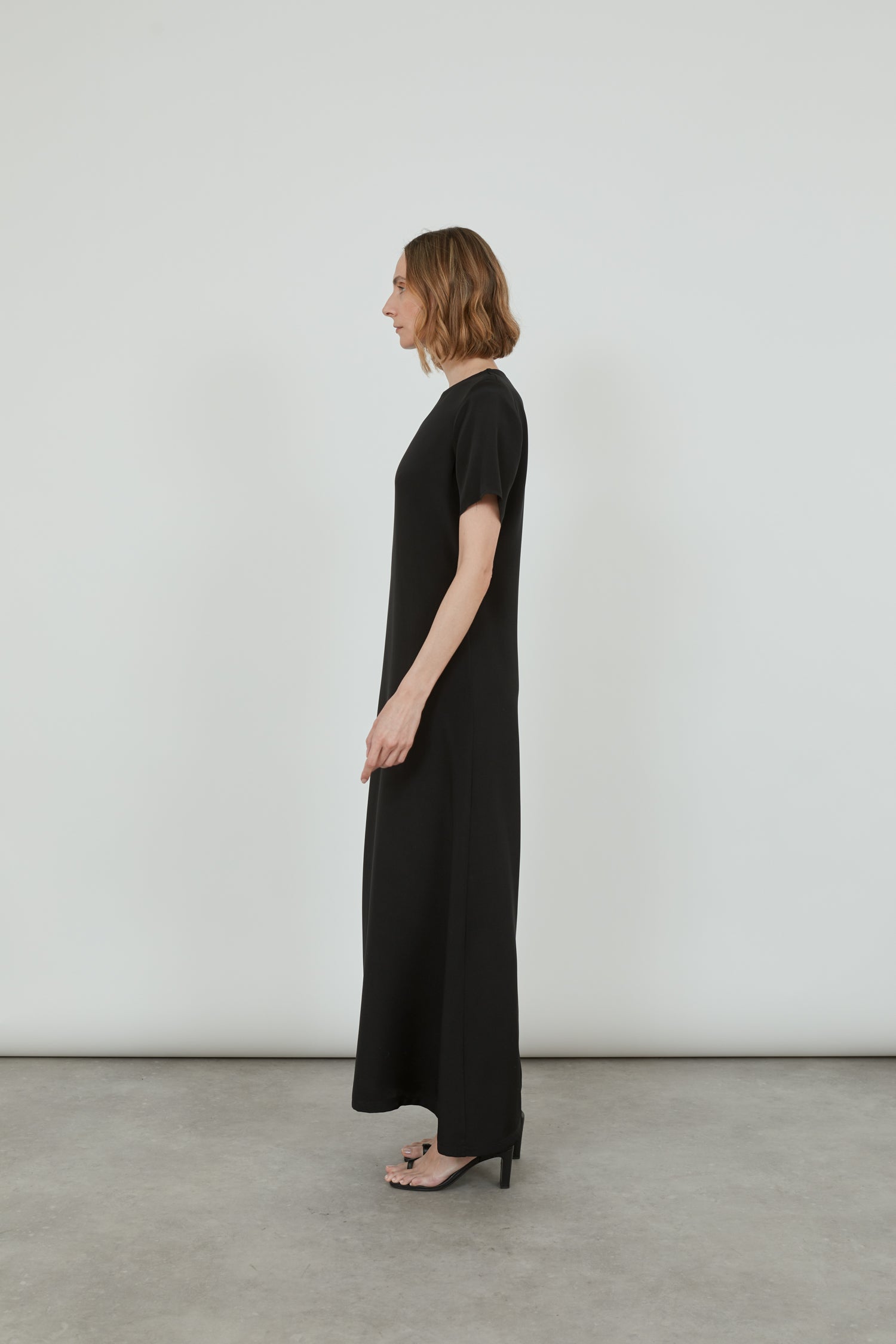 Side view of the black Celine dress, showcasing its smooth crepe silk fabric and the raw hem detailing on the sleeves.