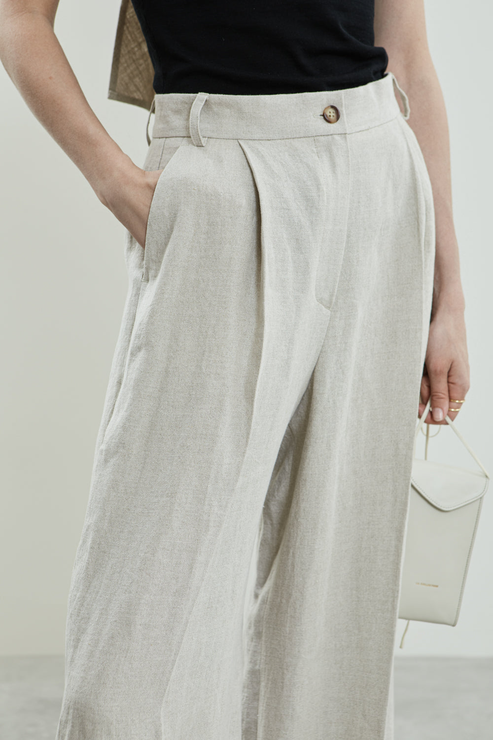 Close-up of the soft pleats and linen fabric of the beige Dalida trousers.