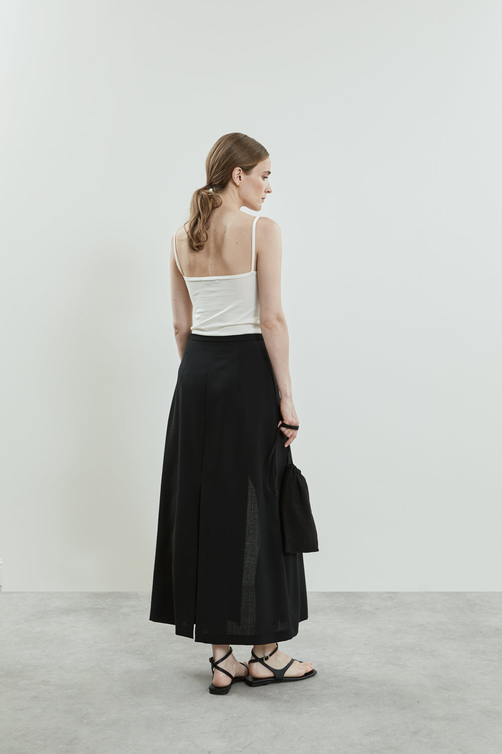 Back view of the black Donna skirt in virgin wool, emphasizing the sleek silhouette and contemporary splits at the back.