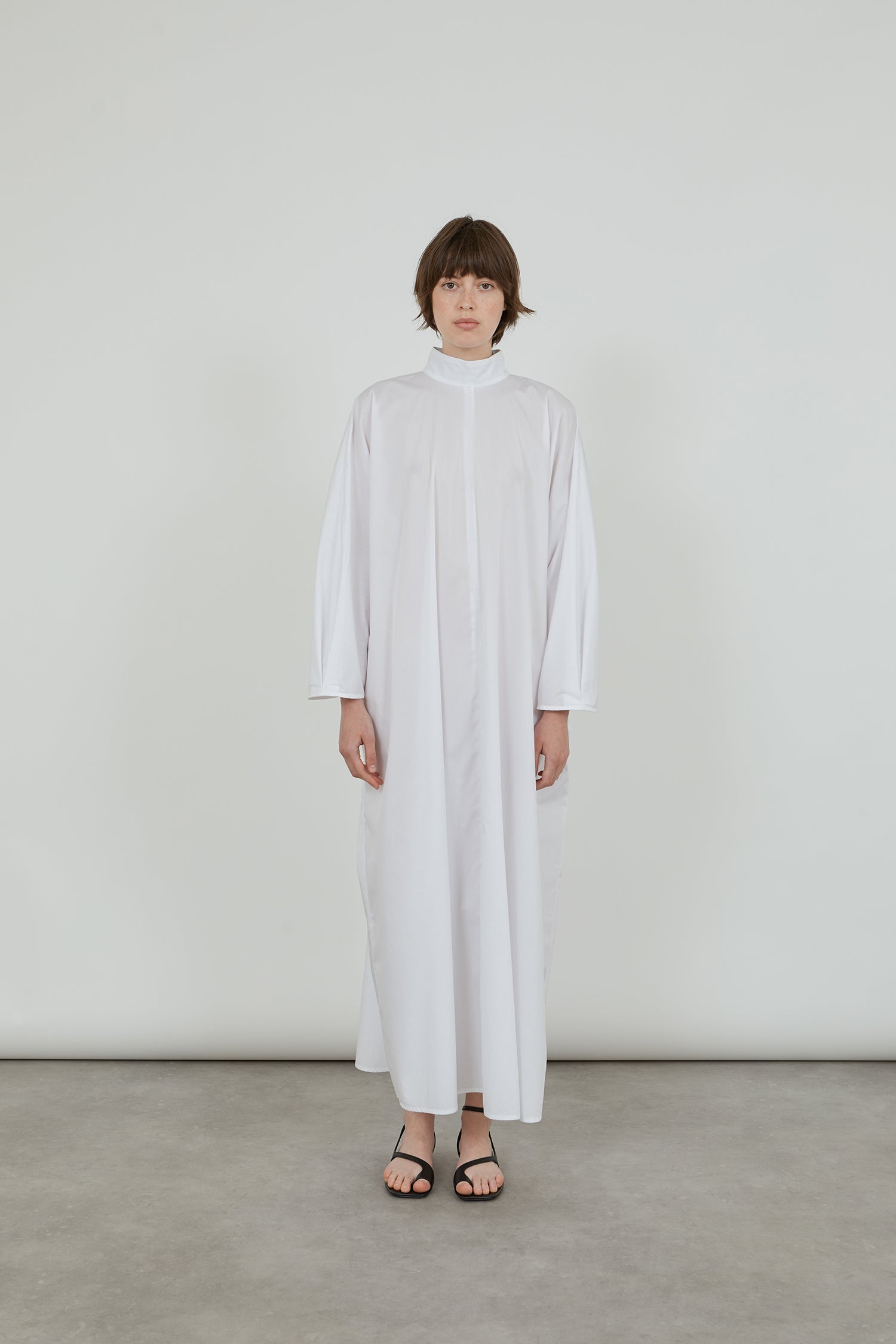 Front view of the white Emiko dress in cotton poplin, showcasing the effortless kaftan design with a loose fit, featuring a collar, button closure at the back, and dolman sleeves.