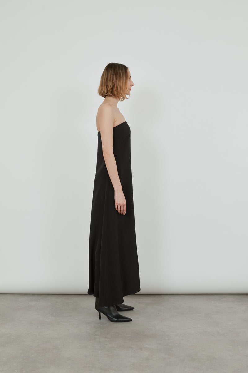 Woman wearing a black bandeau dress standing sideways.
