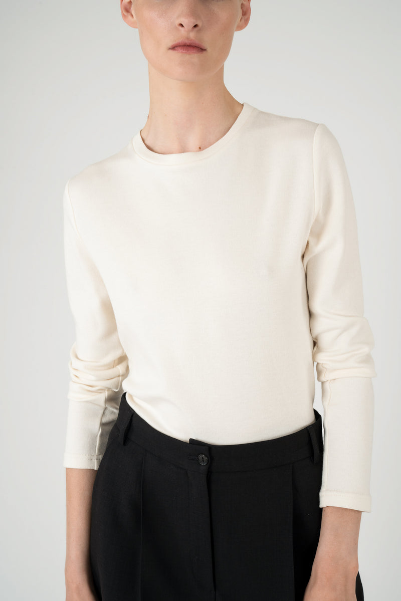 Detailed view of a woman wearing an off white longsleeve top with black trousers.
