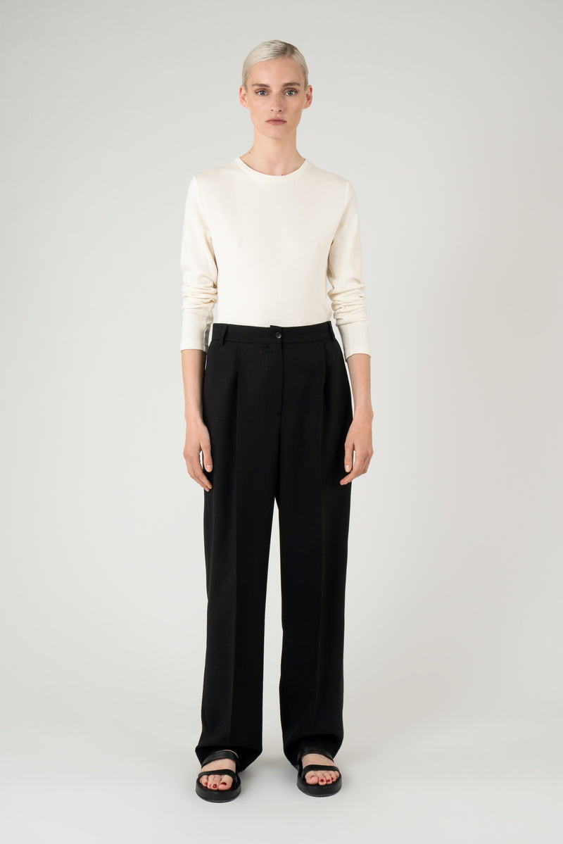 Woman wearing an off white longsleeved top with black trousers and black leathersandals.
