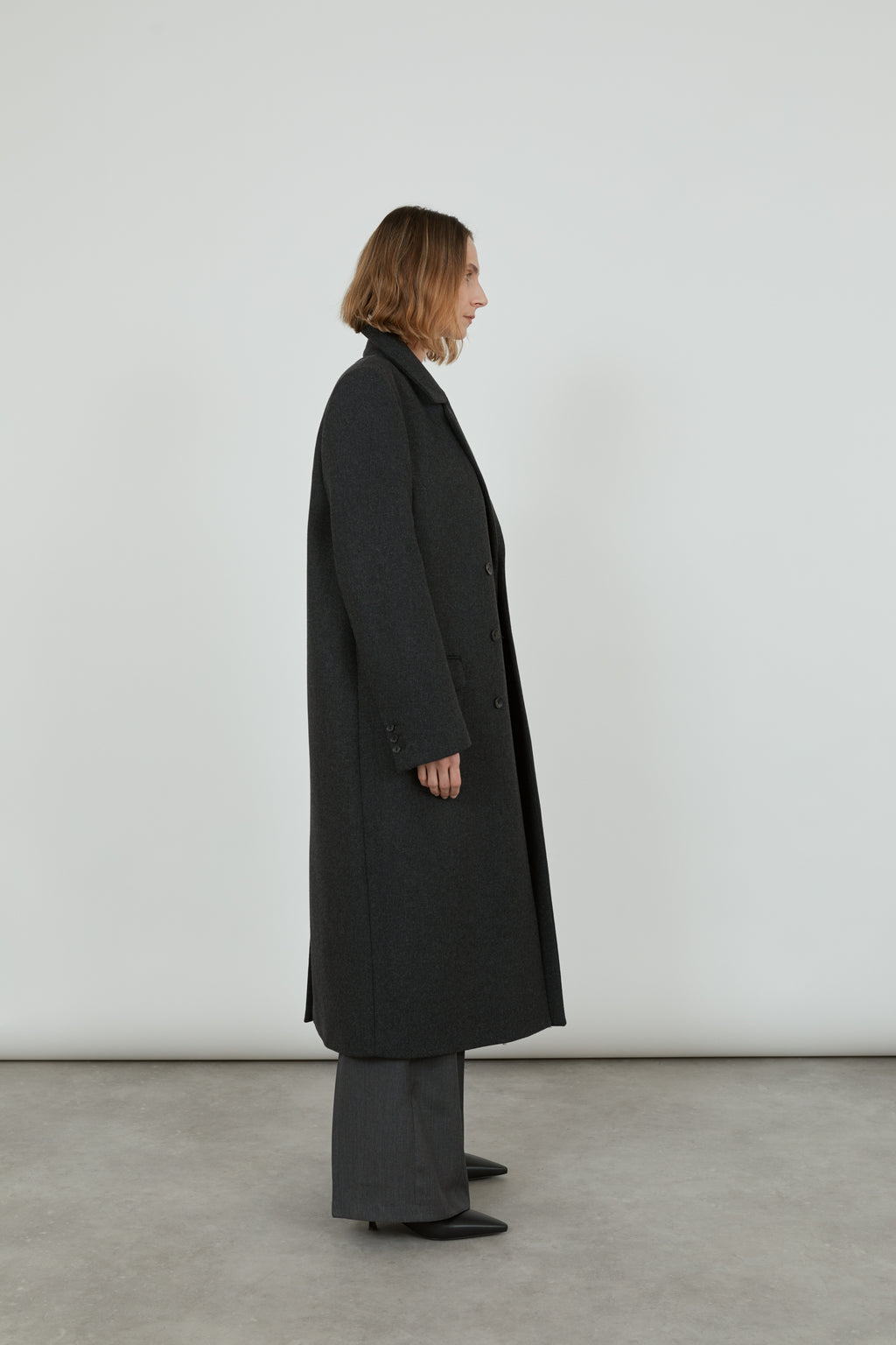 A woman is wearing a dark grey wool winter coat and is looking sideways. 