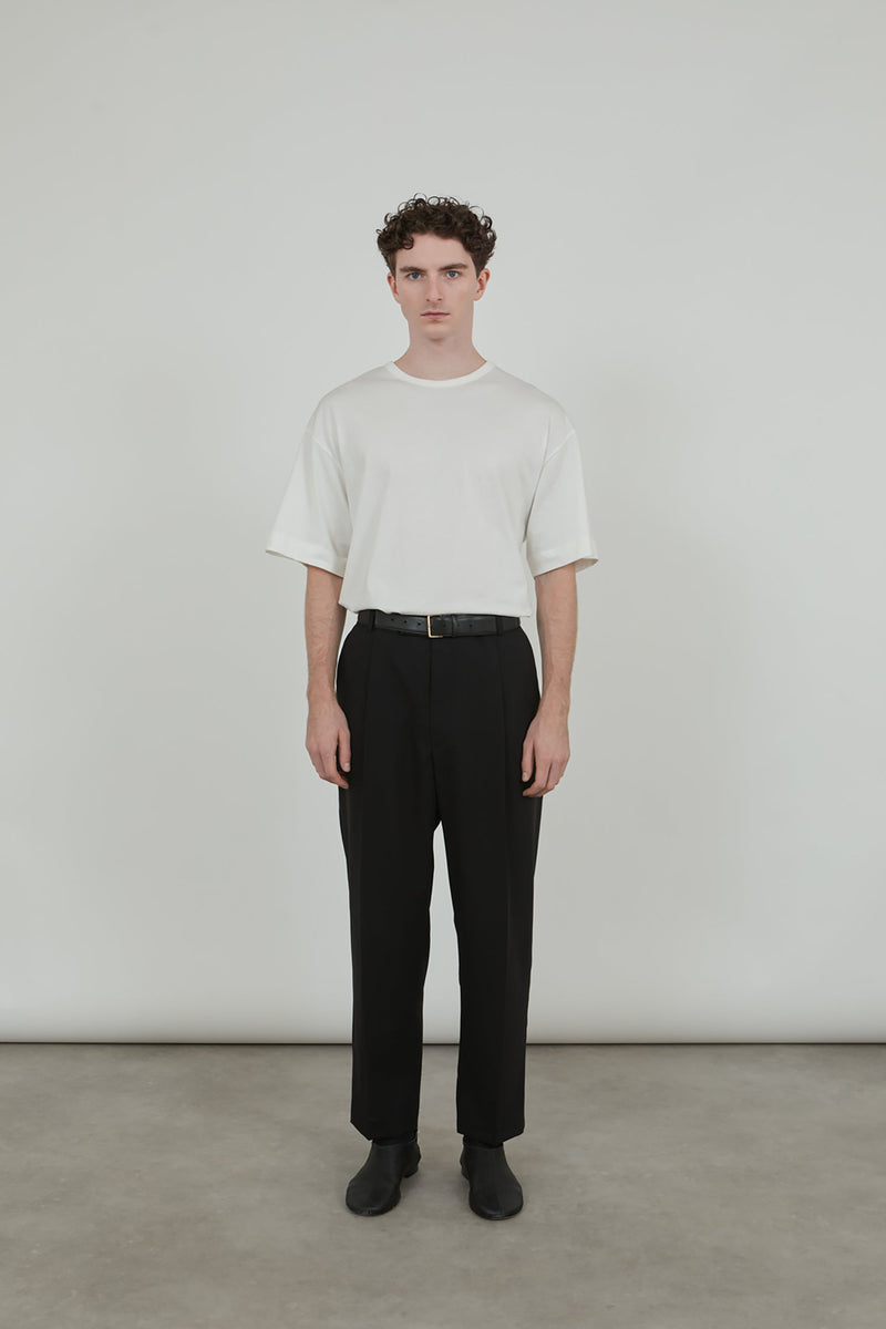 Man wearing white boxy T-shirt on black trousers with black leather belt.