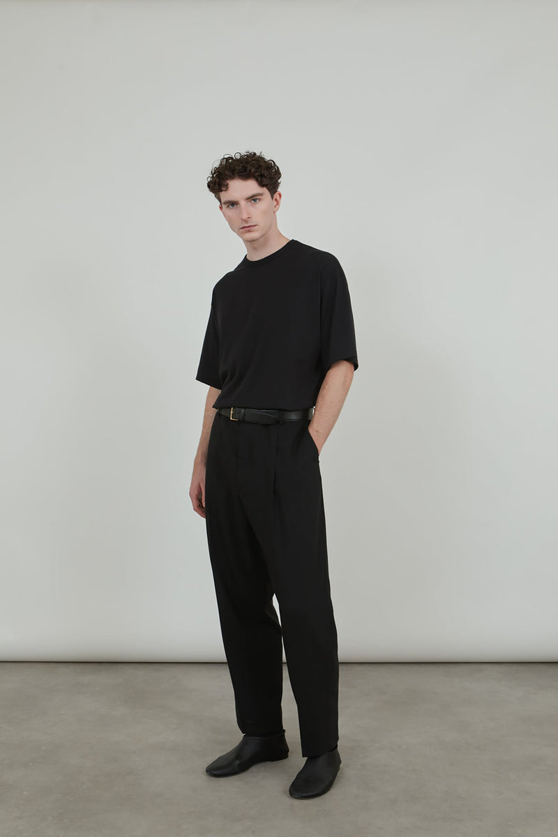 Man wearing a black cotton jersey T-shirt with a black leather belt and black virgin wool pants. 