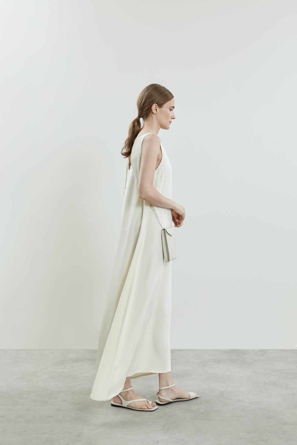 Side view of the Quinn dress in off white crepe silk, showcasing its fluid A-line shape and floor-length drape.