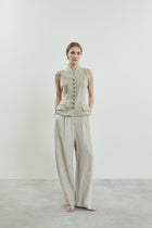 Front view of the Sada trousers in beige linen, featuring a slightly dropped crotch, side pockets, and belt loops.