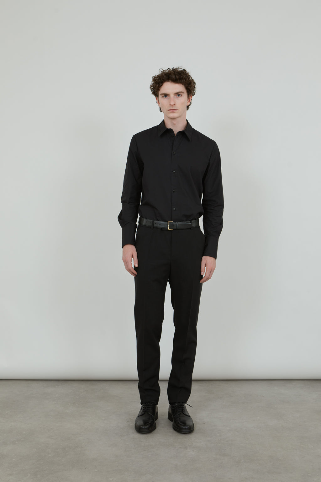 Man wearing a classic black trousers in virgin wool, combined with a classic black shirt and a black leather belt. 