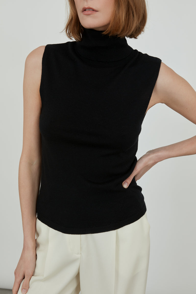 Woman wearing a sleeveless black Deborah knit top in merino wool with classic offwhite pants, from a detailed view.