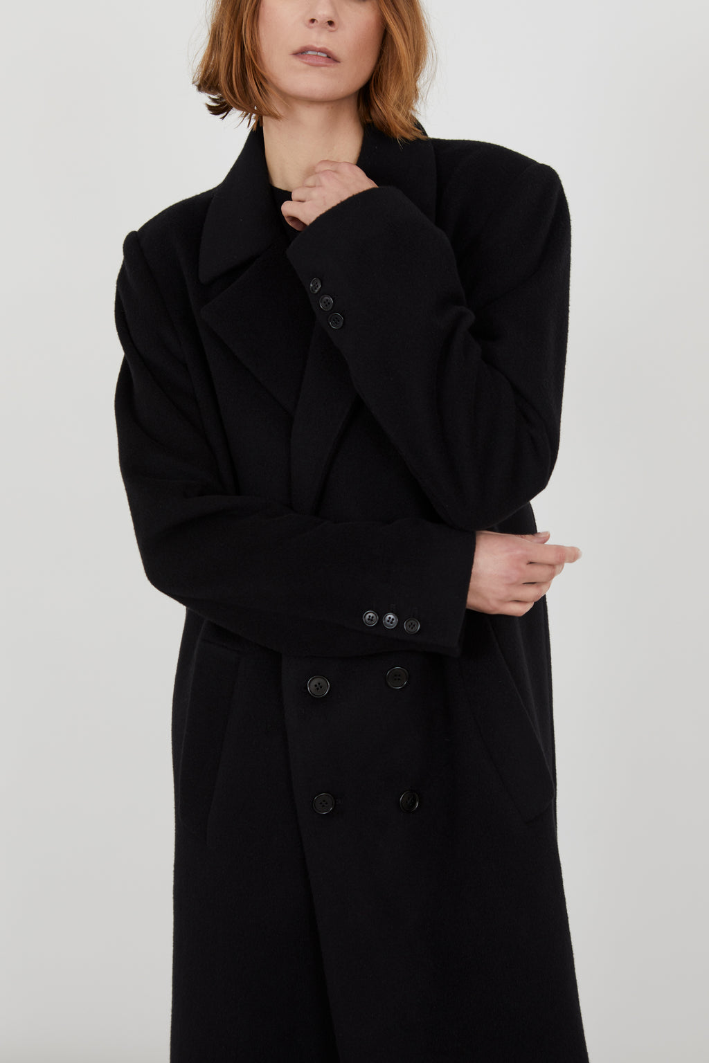 A person wearing a black cashmere coat. Focus on the buttons