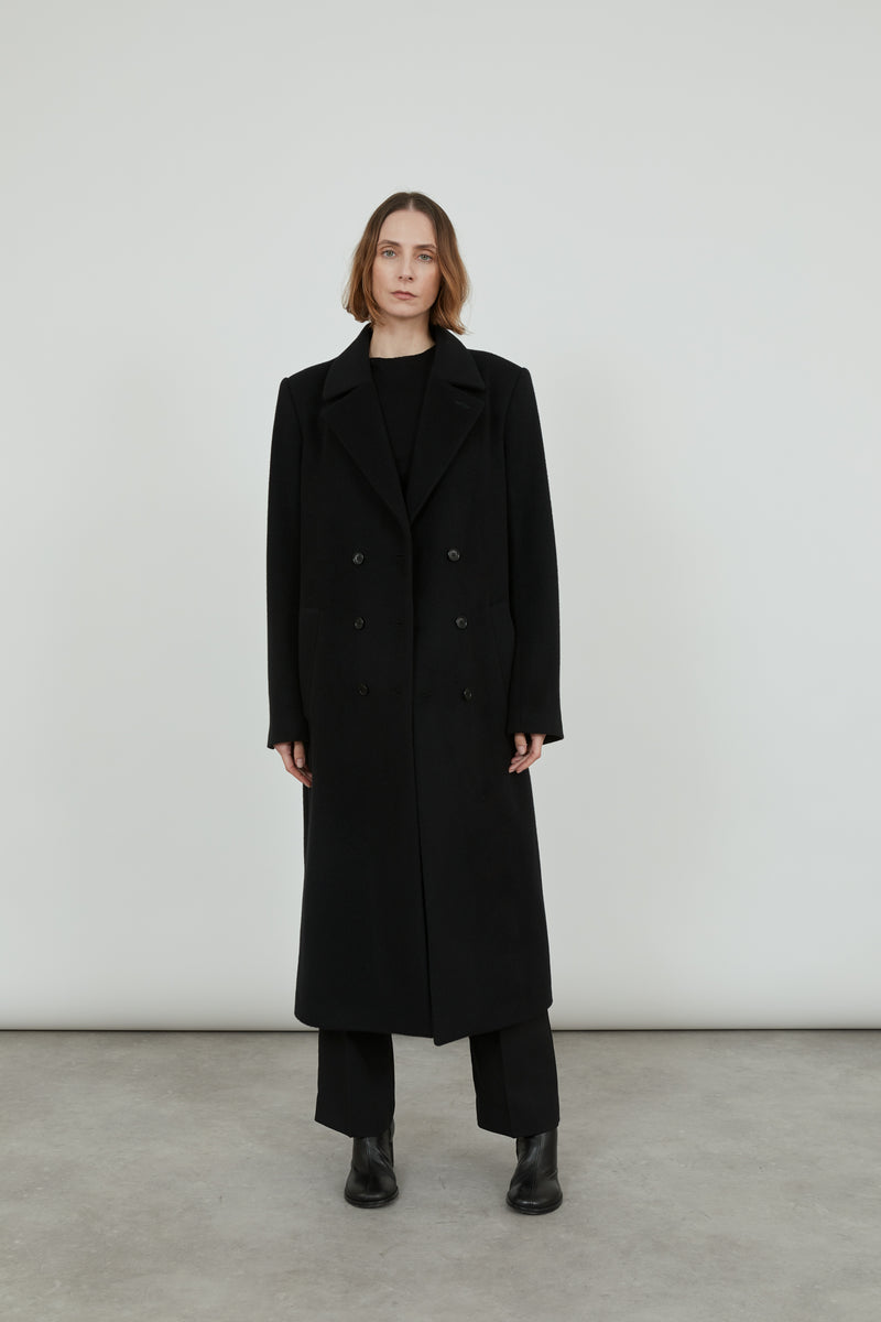 A person wearing the black Achilles coat in cashmere wool..