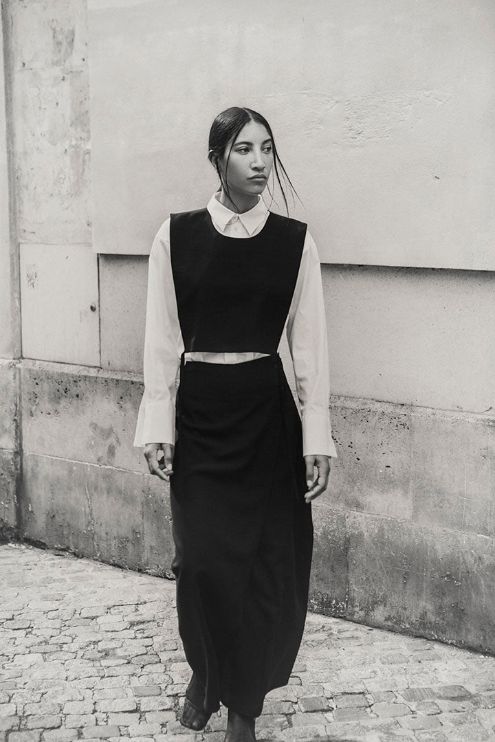 Woman wearing the black Mireille top over a white cotton shirt  with a long black skirt.