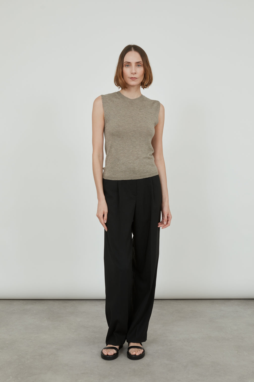 Woman wearing a sleeveless biscuit Emma knit top in merino wool with classic black pants and black leather sandals. 