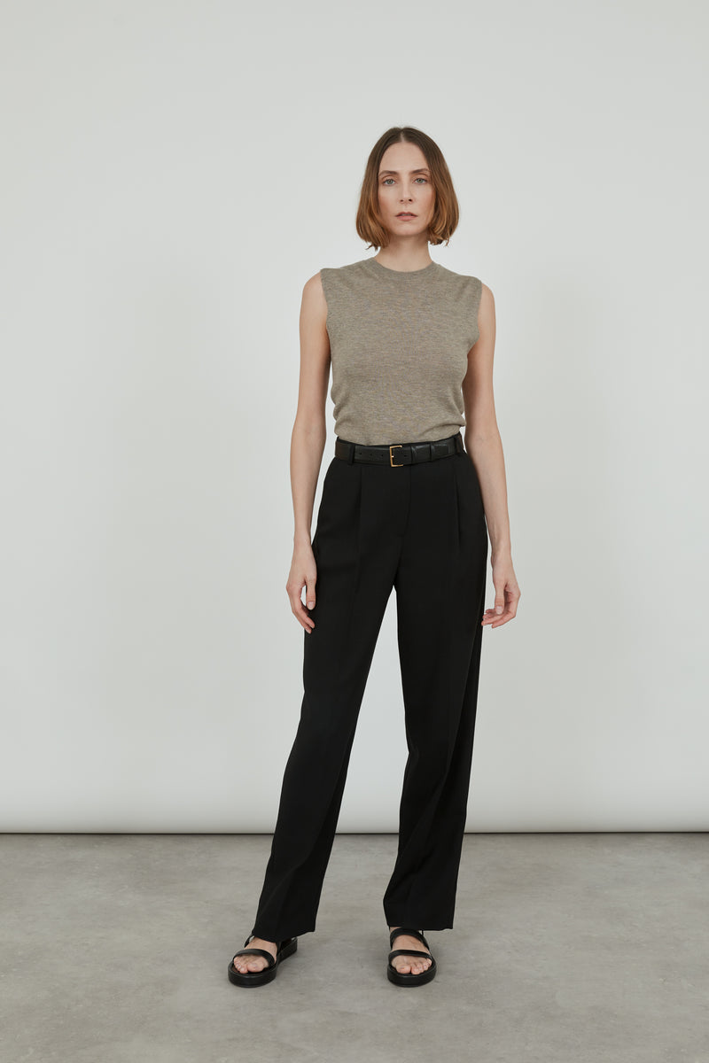 Woman wearing a sleeveless biscuit Emma knit top in merino wool with classic black pants, black leather sandals and a black leather belt. 
