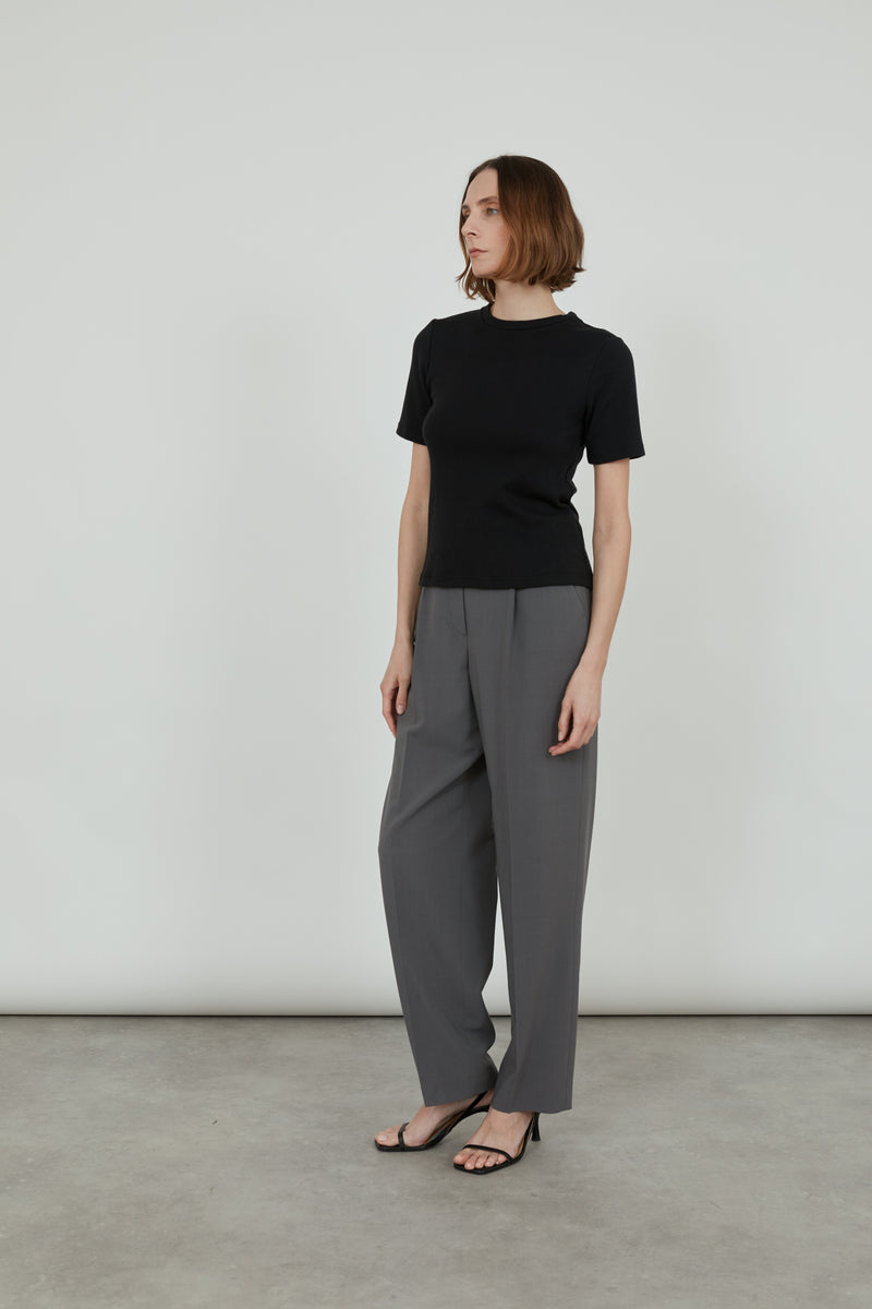 Woman wearing a black organic cotton T-shirt and a grey pants standing sideways.