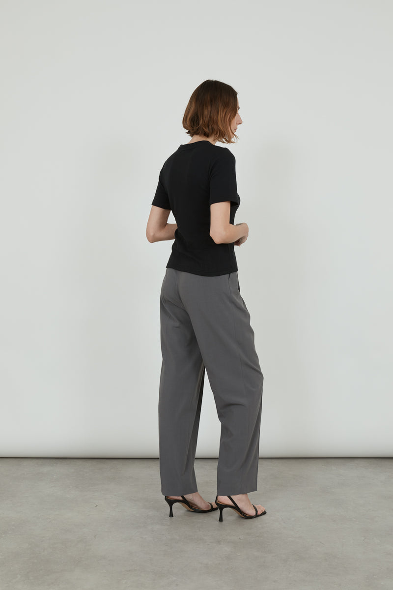 Woman wearin black T-shirt, grey trousers and black leather sandals, showing her back. 